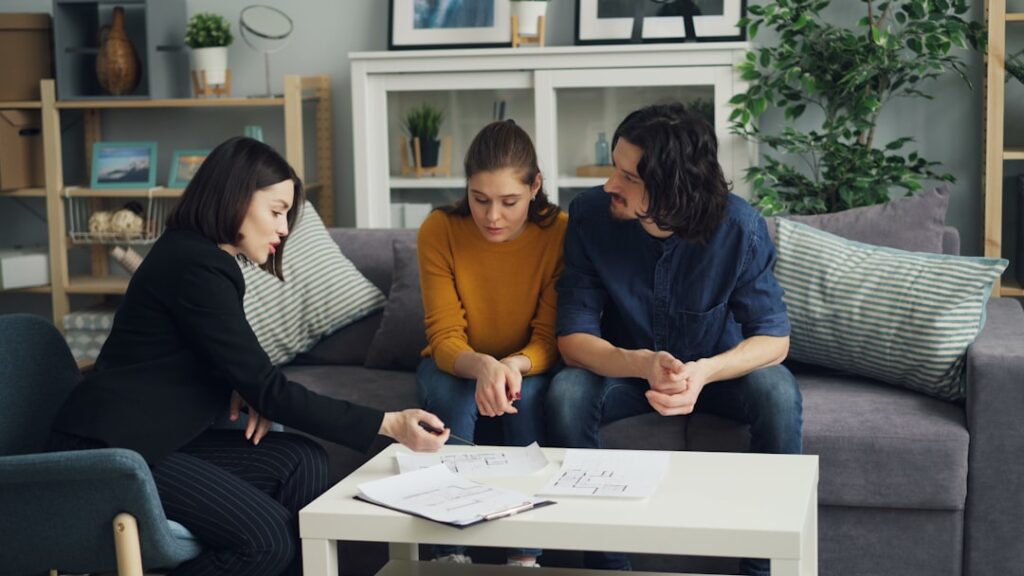Two adults review insurance documents at a kitchen table, surrounded by photos of home water damage.