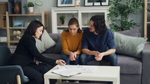 Two adults review insurance documents at a kitchen table, surrounded by photos of home water damage.