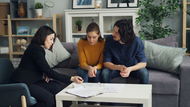 Two adults review insurance documents at a kitchen table, surrounded by photos of home water damage.