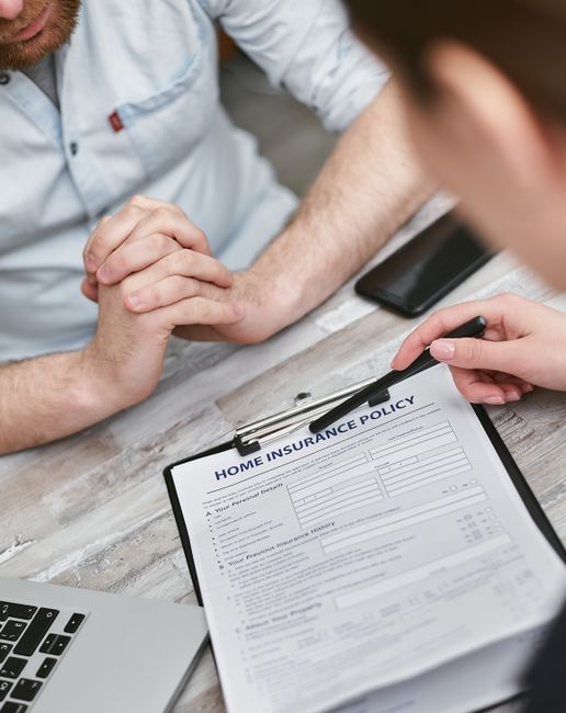 A concerned family reviews insurance papers together at their dining table, paperwork and a laptop spread out.