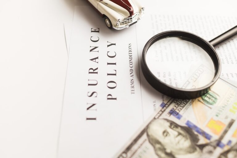 A person at a kitchen table organizing insurance claim documents and paperwork with a laptop and phone.